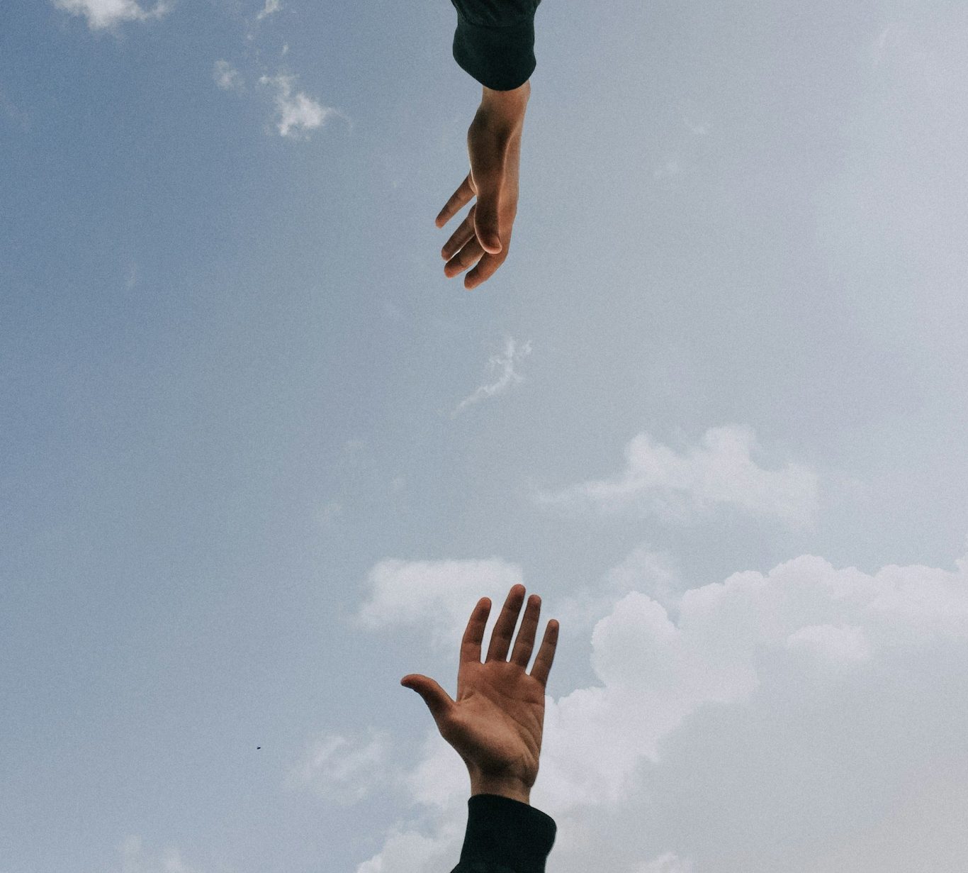 Zwei Menschen versuchen sich die Hände zu reichen Bild von zwei Händen vor blauem Himmel mit leichter Bewölkung